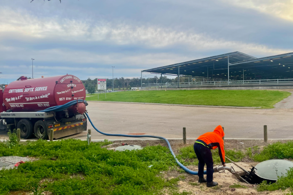 Operator in hi-vis connecting the tanker hose to a septic tank beside a racecourse