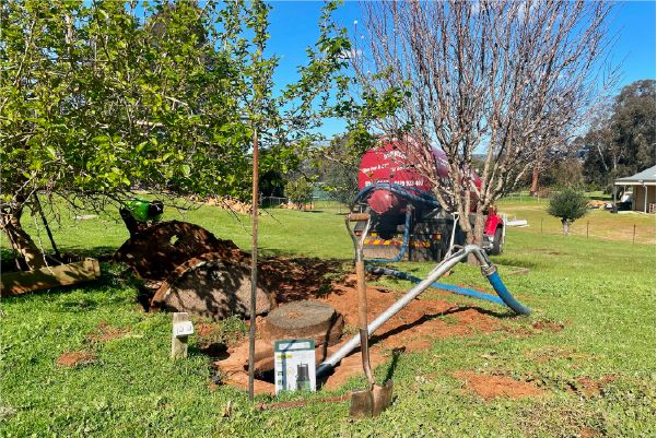 Tanker hose running to an excavated sump on a grassy rural block